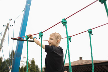 the boy goes through an obstacle course is engaged in active sports holding on to ropes to make his way to the finish line