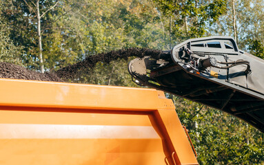 Road milling machine removes asphalt from old road and loads milled asphalt in dump truck.  © andrew_shots