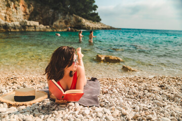 woman in red swimsuit laying on blanket at sea beach reading book