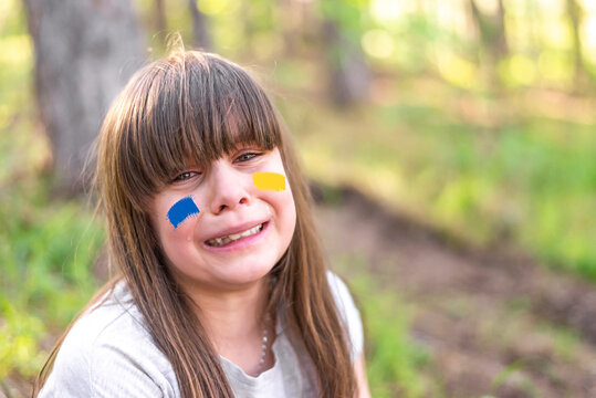 Scared child with devastated life crying in the woods, running from war. Sign of Ukrainian flag on child's cheek. Ukrainian geopolitics globe crisis. Close up kids face. Sadness longing hope. No war. 