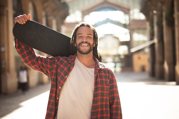 Portrait of young handsome guy with skateboard. Happy smiling skater outdoors..