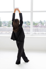 Portrait of a woman inside a studio with a grey background wearing a black suit with black high heels and a black bra.