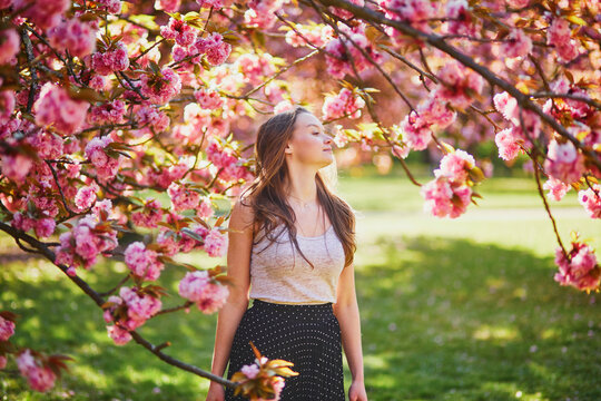 Beautiful young woman on sunny spring day in park during cherry blossom season