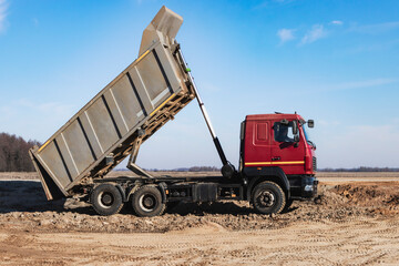 A large mining truck unloads the earth. A soil transporter with a raised body dumps soil.
