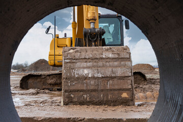 Heavy excavator at the construction site. View of the excavator through the iron pipe. Construction...