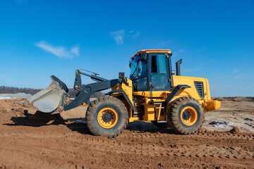Obraz na płótnie Canvas Bulldozer or loader moves the earth at the construction site against the blue sky. An earthmoving machine is leveling the site. Construction heavy equipment for earthworks.