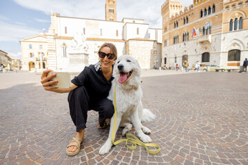 Woman takes selfie photo with dog traveling in Grosseto town the center of Maremma region in Italy....