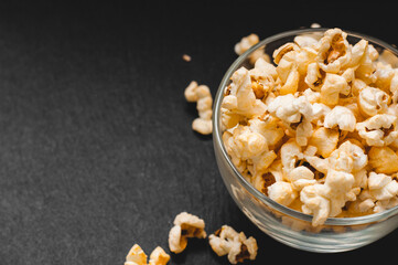 Glass bowl with cheesy popped popcorn on dark black background