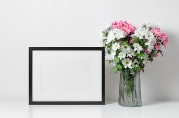 Picture frame mockup in white minimalistic interior with flowers bouquet.