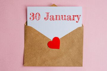 Kraft envelope with a white sheet of paper and a date 30 january, with a red heart. Flat lay on pink background, romance and love concept