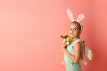 Obraz na płótnie Canvas Beautiful cute little girl in Easter bunny ears smiling and holds easter decor on a pink background. Copy space. Easter postcard