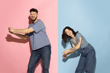 Young excited couple of funny and happy man and girl dancing hip-hop, having fun isolated on blue and pink trendy color background. Emotions concept