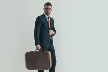 grizzled hair man in his forties buttoning suit and holding luggage