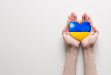 Two hands holding yellow and blue heart, national Ukraine flag. Help to Ukraine. Aid to refugees. Place for text.