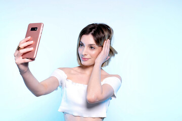 Photo of young caucasian girl with light blue eyes who takes selfie with her smartphone - Studio photography of pretty woman holding her phone photographing herself