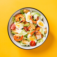 Fresh Shrimp Caesar Salad with parmesan cheese and Croutons. Yellow background, top view.