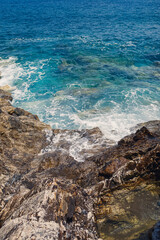 Wonderful views of the blue Mediterranean Sea. Sunny rocks, waves with foam and splashing water. The wave crashes into the rocks on the shore
