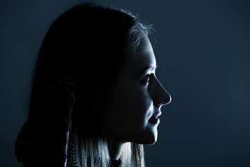 Close-up woman with feathers in her hairs dark profile portrait. Model face partly illuminated by blue light imitating television or moon light. Selective focus and image with shallow depth of field © Rytis