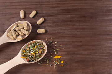 Organic pills on wooden spoon wiht herbals on wooden background.