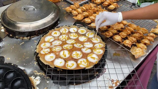 Street vendor prepares Khanom Khrok, a traditional Thai dessert in form of pancakes, made with coconut milk, rice, flour, sugar and other ingredients in Bangkok, Thailand.