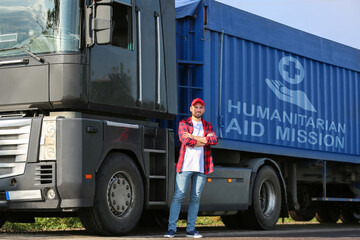 Driver near truck with inscription HUMANITARIAN AID MISSION on road. Stop war in Ukraine