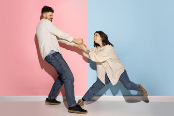 Emotional couple of young funny and happy man and girl having fun studio on blue and pink trendy color background.