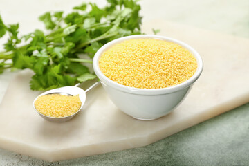 Bowl and spoon with raw couscous with parsley on grunge background