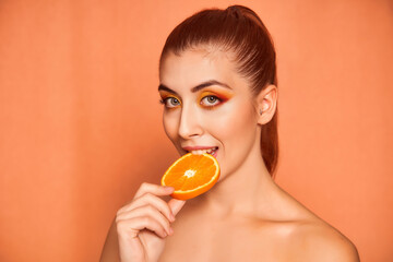 Portrait of beautiful young woman biting an orange on yellow background. High quality photo