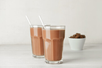 Glasses of delicious chocolate milk on white wooden background
