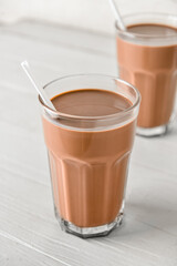 Glass of delicious chocolate milk on white wooden background