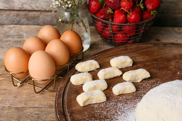 Board with raw lazy dumplings and chicken eggs on wooden background, closeup