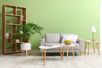 Interior of light living room with grey sofa, tables and fruit basket
