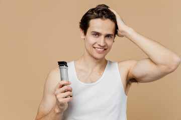 Attractive young man 20s perfect skin wear undershirt hold electric razor grooming with trimmer...