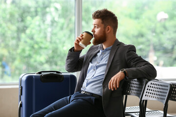 Handsome businessman with suitcase drinking coffee in hall of airport