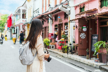 Happy Asian traveler woman take a photo while walking on the city street. Travelling in Phuket Old Town in Thailand concept - obrazy, fototapety, plakaty