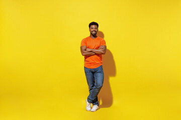 Fototapeta na wymiar Full body young smiling fun happy man of African American ethnicity 20s in basic orange t-shirt hold hands crossed folded isolated on plain yellow background studio portrait. People lifestyle concept.