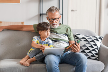 Senior man reading story to his little grandson on sofa at home