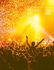 Draagtas A crowded concert hall with scene stage orange and yellow lights, rock show performance, with people silhouette, colourful confetti explosion fired on dance floor air during a concert festival © tsuguliev