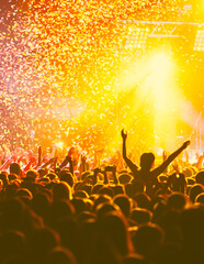 A crowded concert hall with scene stage orange and yellow lights, rock show performance, with people silhouette, colourful confetti explosion fired on dance floor air during a concert festival - obrazy, fototapety, plakaty