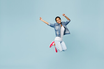 Full size happy exultant little kid teen girl of African American ethnicity 12-13 year old in denim jacket jump high stretch hands isolated on pastel plain light blue background. Childhood concept