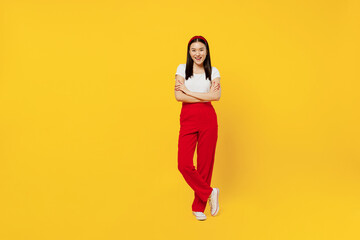 Fototapeta na wymiar Full size body length smiling fun young girl woman of Asian ethnicity 20s years old wears casual clothes looking camera smiling keep hands crossed isolated on plain yellow background studio portrait.