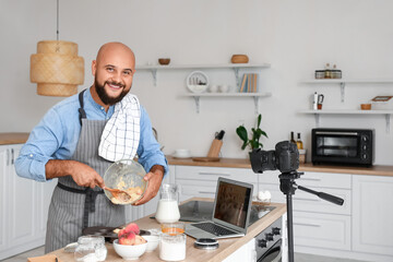 Handsome man preparing peach muffins and recording video tutorial in kitchen