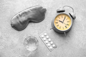Sleep mask, alarm clock, glass of water and pills on grey background
