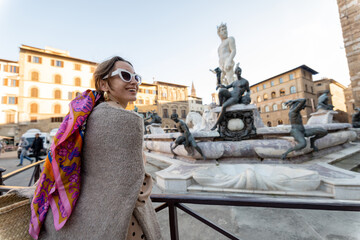 Fototapeta na wymiar Young woman traveling famous italian landmarks in Florence city. Enjoying beautiful architecture and Neptuine fountain on Signoria square. Woman dressed in Italian style with colorful scarf in hair