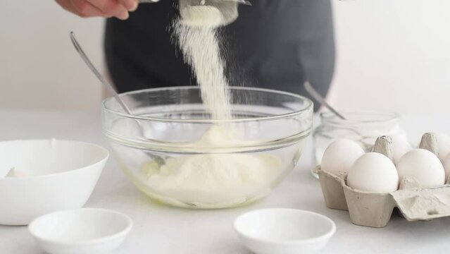 Process of making dough cake. woman’s hands sift flour. On the side stand milk, eggs and in bowl sugar on white table. ingredients for baking cake in kitchen, recipe. flour pour out of a sieve