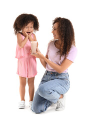 Surprised little African-American girl and her mother with glass of sweet cocoa on white background