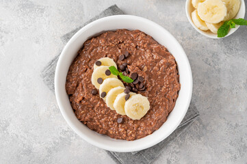 Chocolate oatmeal porridge with banana and chocolate chips on top in a white bowl. Healthy...