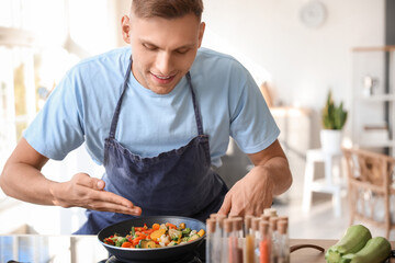 Young man frying tasty vegetables in kitchen