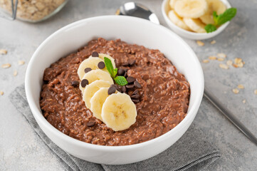 Chocolate oatmeal porridge with banana and chocolate chips on top in a white bowl. Healthy breakfast. Copy space.