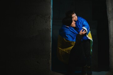 Sad mother hugging her son, both wearing Ukrainian national colors on black background.